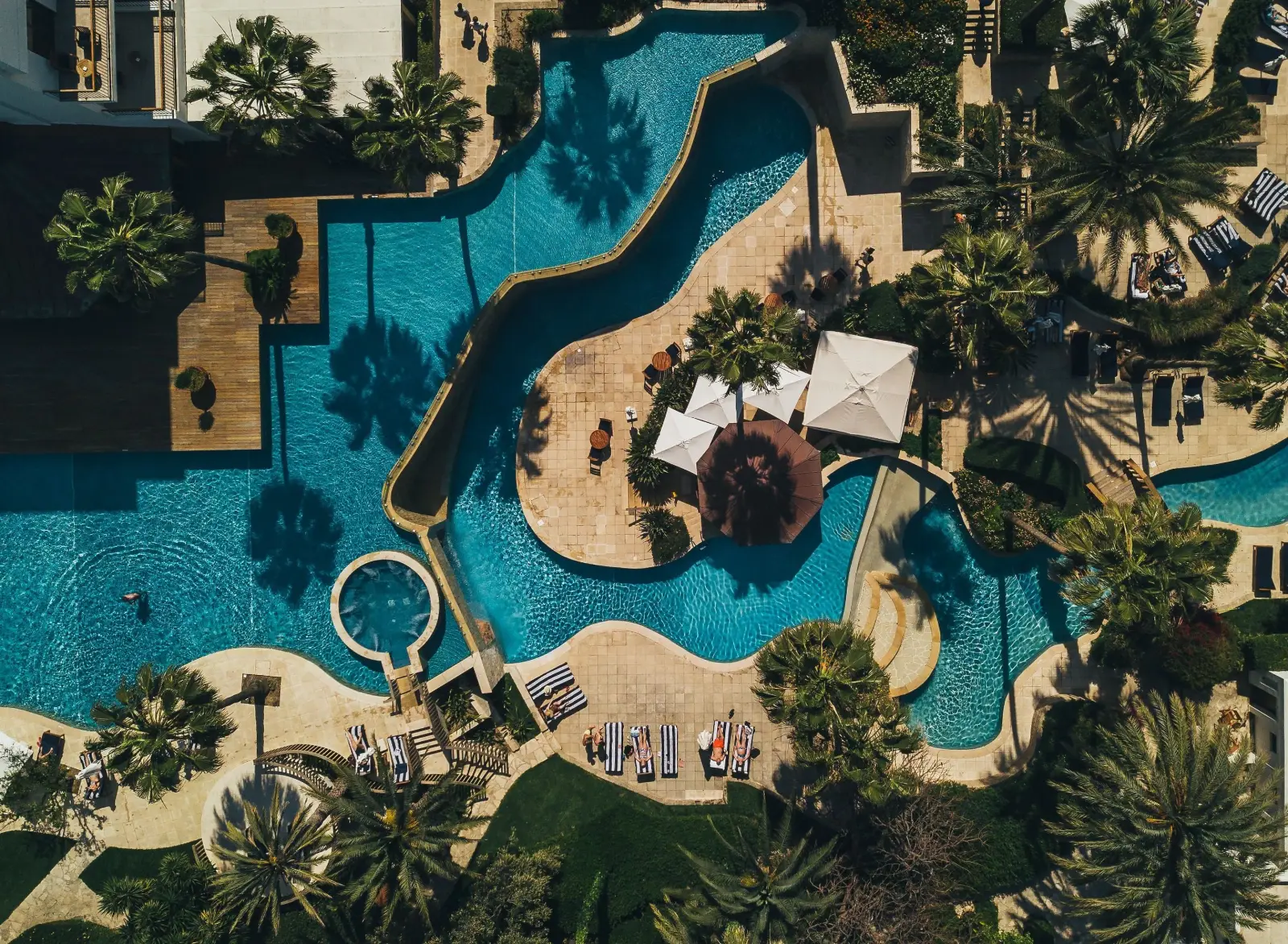 Vogelperspektive auf eine weitläufige Hotelpoolanlage mit Liegen, Sonnenschirmen und Palmen in Paphos.