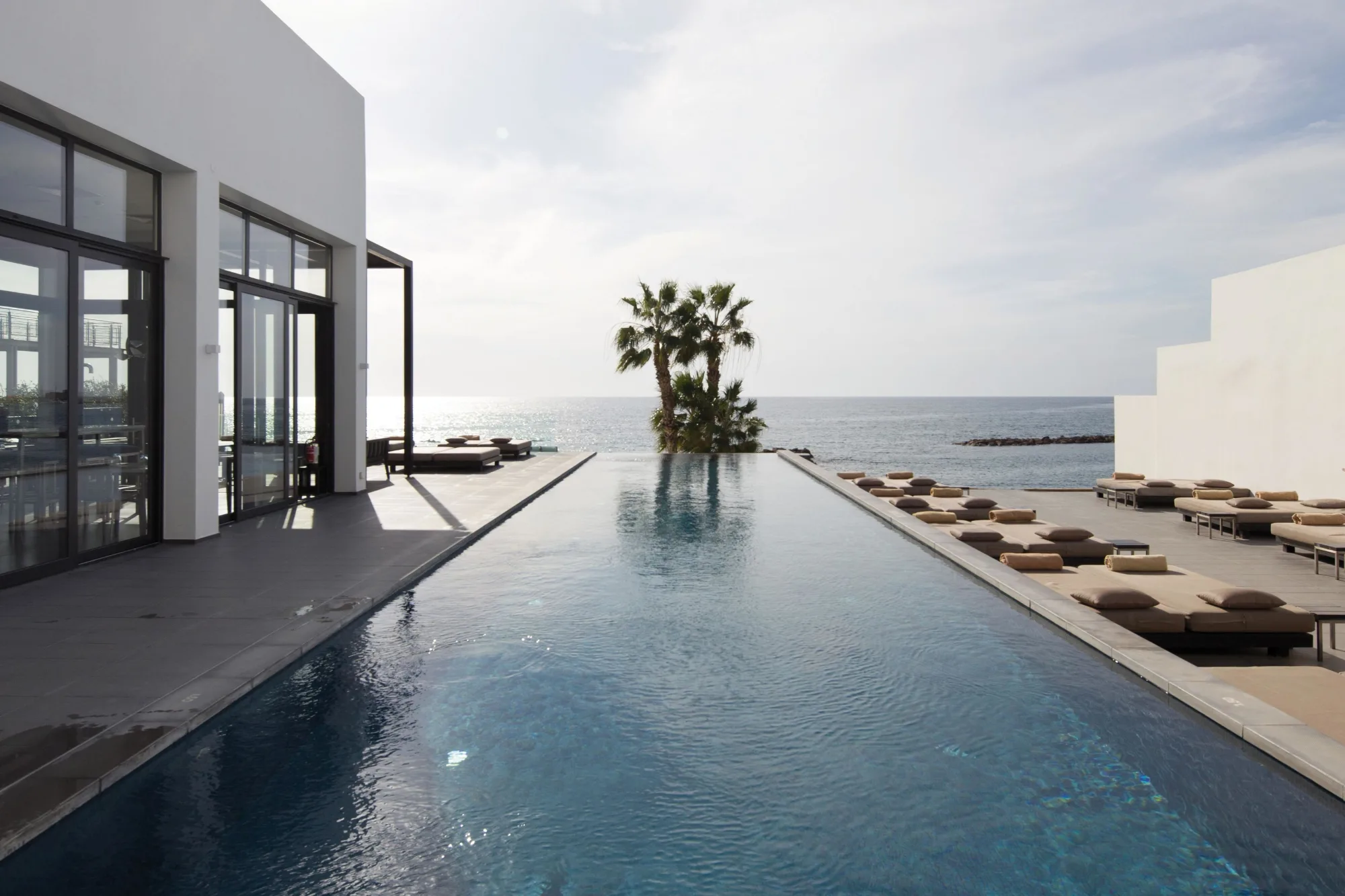 Moderner Infinity-Pool mit Blick auf das Meer und Sonnenliegen am Rand.