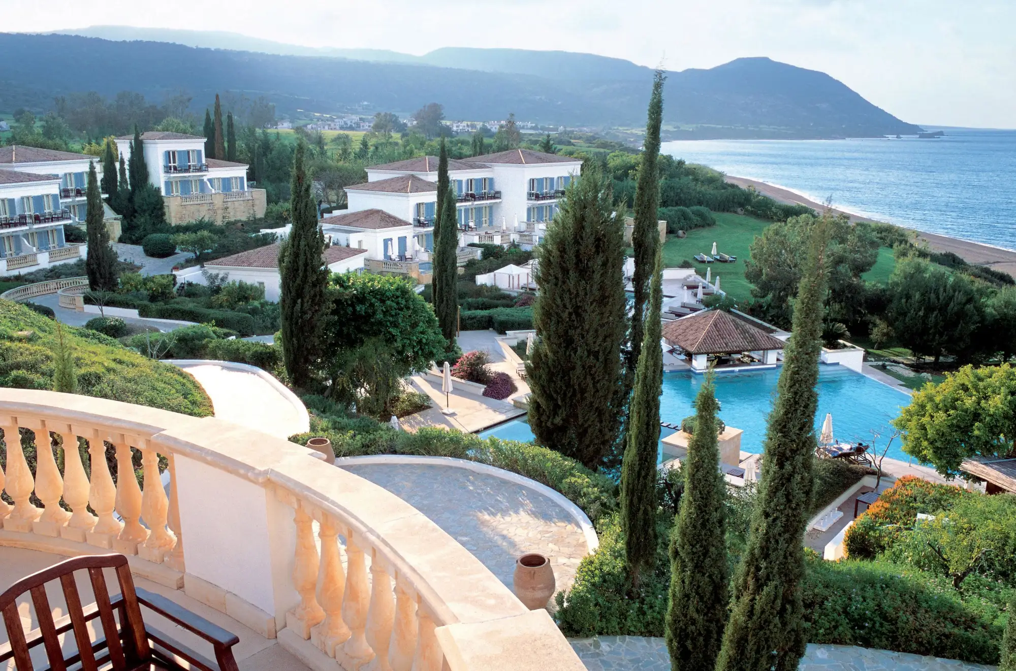 Blick von einem Balkon auf ein Hotelresort mit Pool, Zypressen und Meerkulisse in Neo Chorio, Zypern.