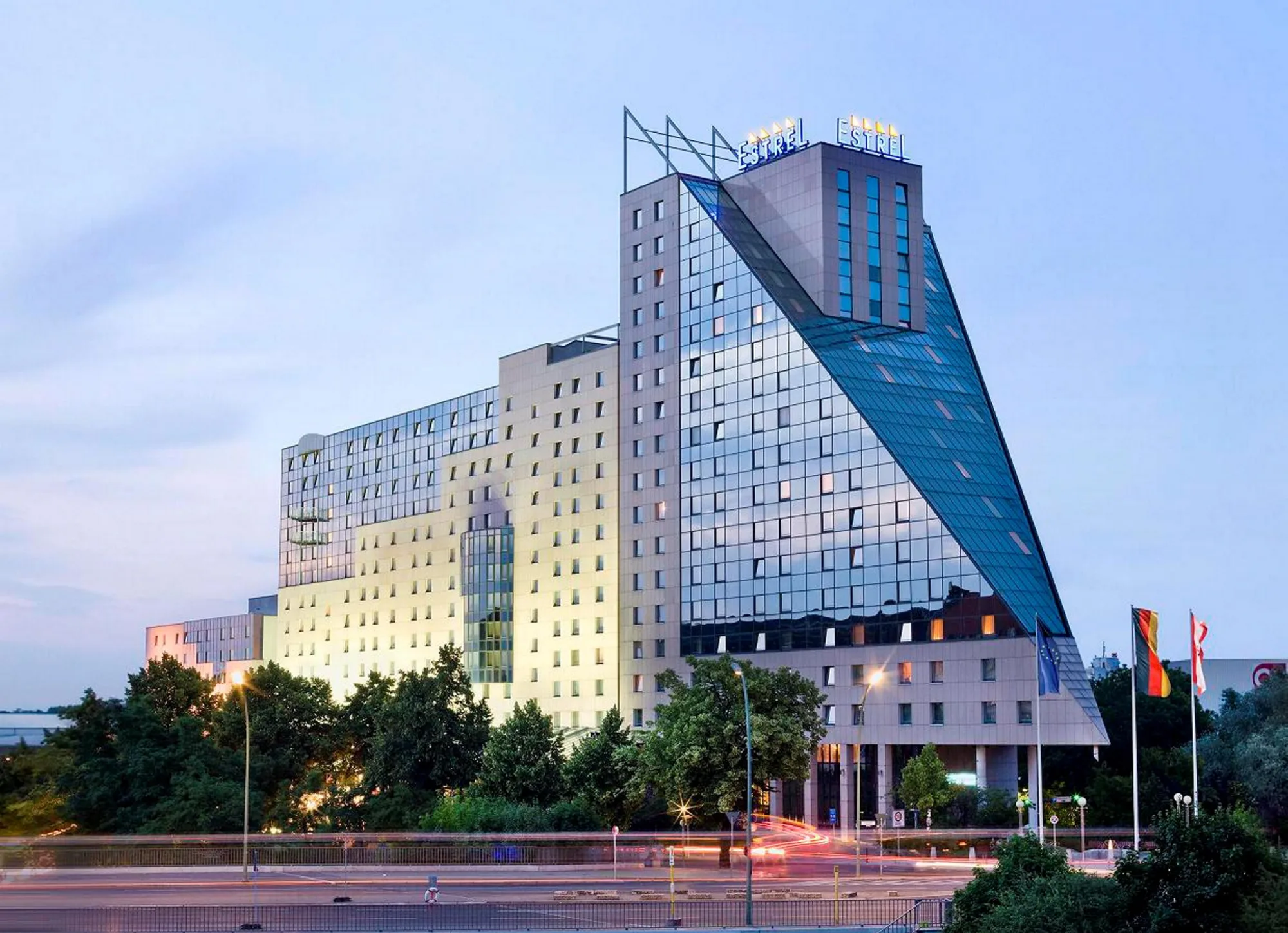 Das Hotel Estrel Berlin bei Dämmerung mit moderner Glas- und Betonfassade und beleuchteten Fenstern.